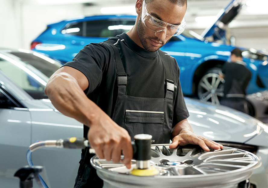 BMW Trained Technician repairs a rim on a service work station near a BMW vehicle in a BMW Certified Collision Repair Center.